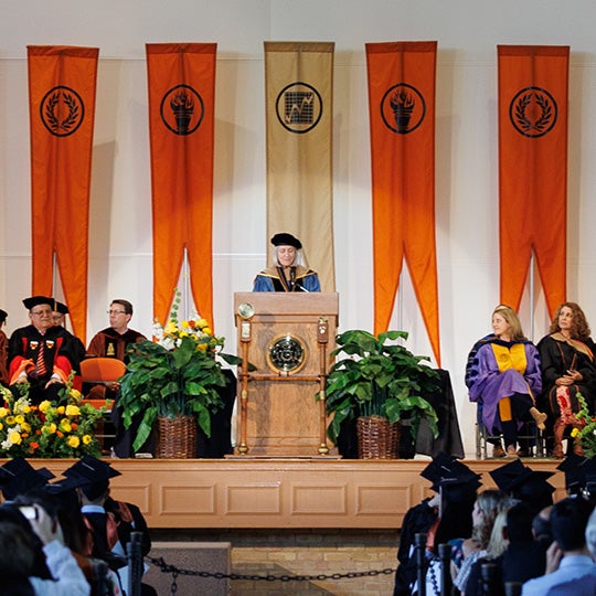 Dean Mills speaking at podium surrounded by fellow faculty